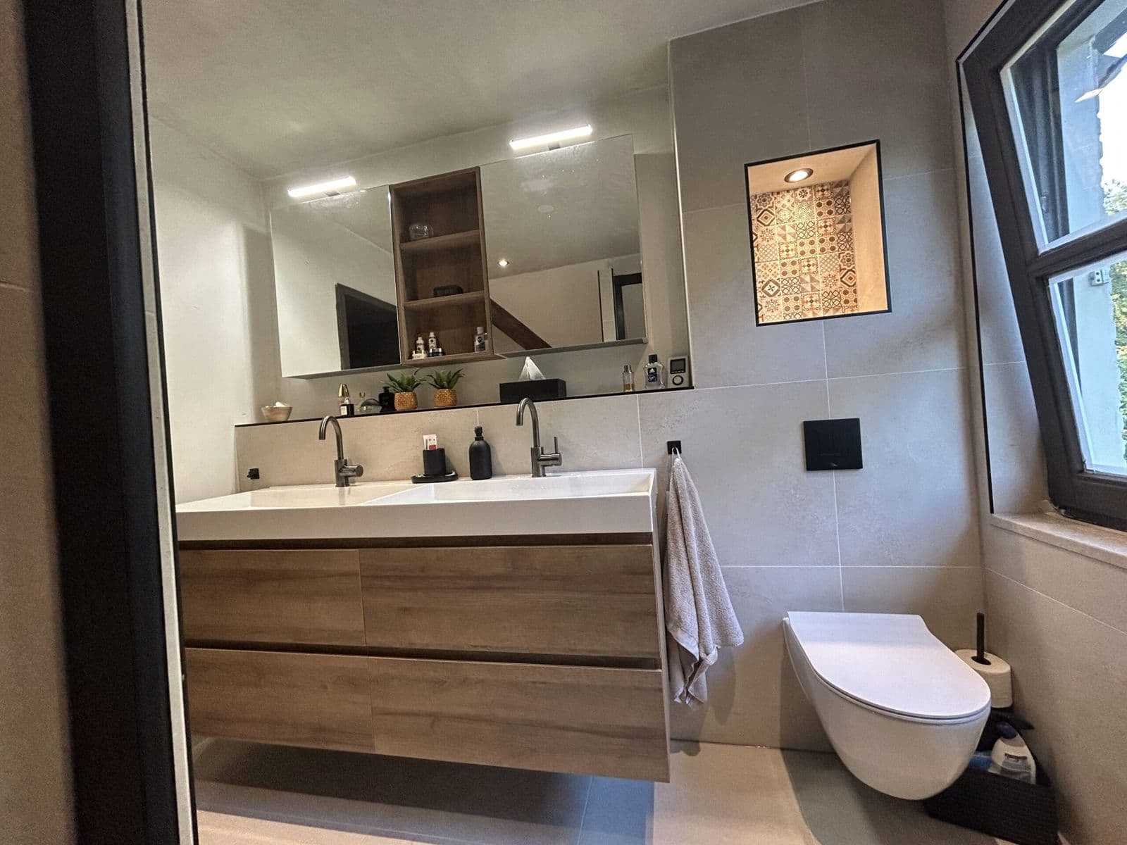 Badkamer met verlichte nis, houten wastafelmeubel en hangtoilet