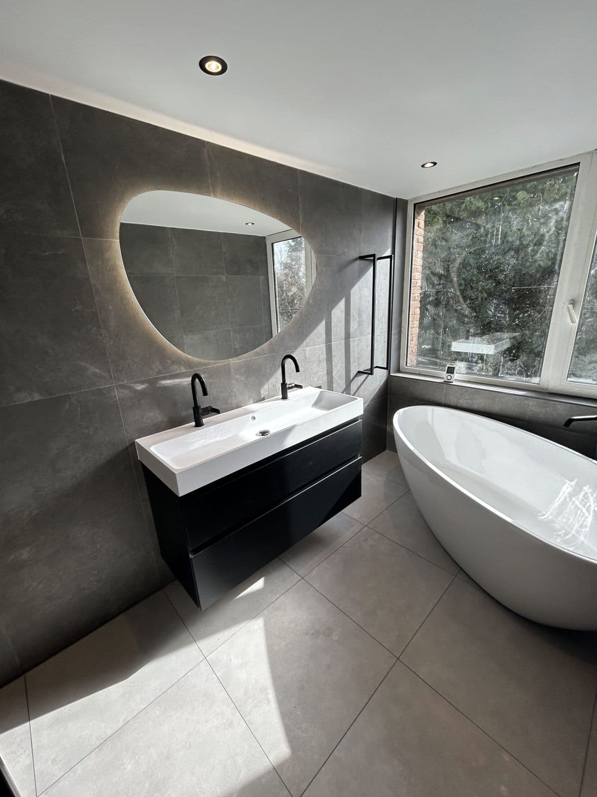 Door Skytec gerenoveerde badkamer met vrijstaand bad, ovale spiegel en zwart wastafelmeubel