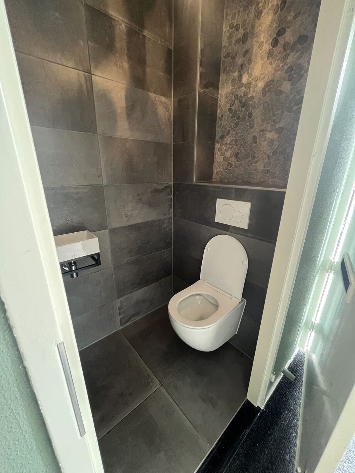 Toilet met donkere tegels, hangtoilet en fontein